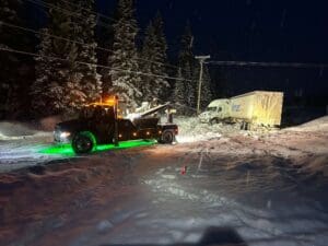 A tow truck is parked in the snow at night.